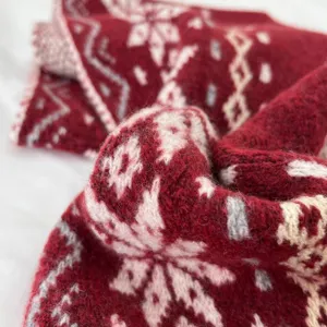 Primo piano dettagliato di una sciarpa in misto lana rossa con motivo a fiocco neve.