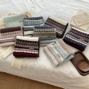 Detailed shot of multi-color Fair Isle knit scarves neatly folded on cozy white bedding.