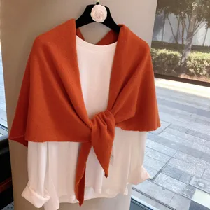 Close-up detail of the cozy orange knit wool shawl paired with white long sleeve top.