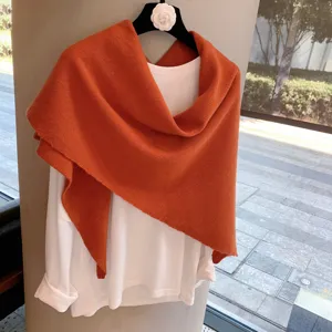 Detail view of the elegant orange knitted triangular shawl paired with white long sleeve top.