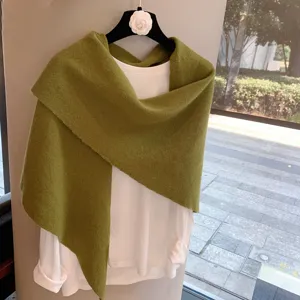 Detailed view of green knitted triangular shawl and white top, cozy winter texture.