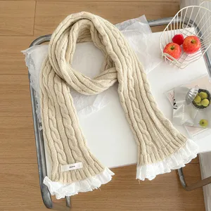 Detail view of cream knitted cable scarf with delicate white lace ruffle trim texture.