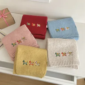 Close-up detail of soft knit winter scarf with cute embroidered horse design and cozy texture.