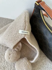 Detailed view of the cozy beige wool balaclava hat featuring cute pom-poms and tag.