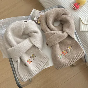 Detailed shot of soft knitted winter scarves with cute horse embroidery in neutral tones.