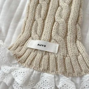 Close-up of cable knit winter scarf featuring delicate white lace trim and woven brand label.