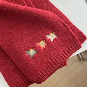 Red knitted scarf detail showcasing cute embroidered cartoon pony motifs and soft warm fabric.