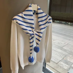 Detailed view of fashionable striped knitted scarf with pom-poms matching a cozy white sweater.