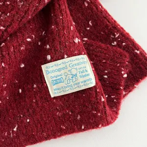 Cozy dark red knit wool scarf detail, soft texture with colorful specks and brand label.