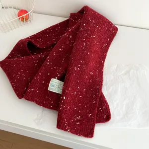 Close-up detail of cozy red knitted wool scarf with colorful speckles and cute label tag.