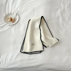 Detailed shot of a cozy white knit winter scarf featuring elegant black contrast scalloped trim.