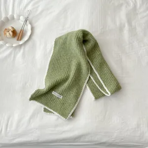 Close-up detail shot of the soft green knitted winter scarf featuring clean white trim and delicate texture.