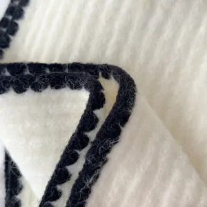 Detailed close-up of soft cozy white knit winter scarf with stylish black contrast edge.