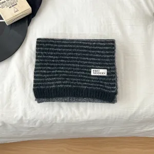 Detailed shot of a black and grey striped knitted scarf displayed on white bed. Cozy winter gear.