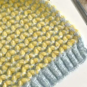 Primer plano detallado de la textura de bufanda de punto grueso amarillo y azul y dobladillo.