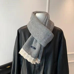 Close-up detail of the cozy gray knitted scarf featuring elegant white lace hem and woven label.