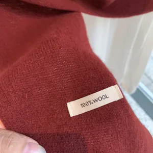 Close-up view of red 100% wool knitted scarf showing soft texture and quality fabric detail.