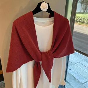 Close-up detail of the red knitted triangular scarf draped over a white long-sleeve top.