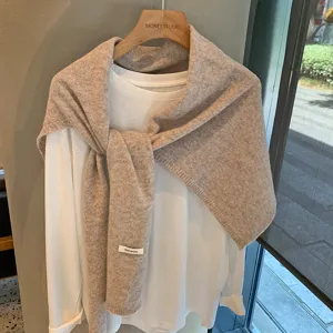 Vista detallada de un elegante chal de lana beige sobre camiseta blanca con percha.