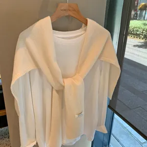 Vista detallada de un elegante chal de punto beige drapeado sobre una camiseta blanca.