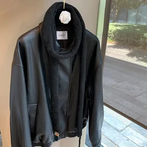 Detailed view of fashionable black leather jacket paired with narrow knit long scarf for women.