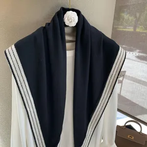 Bufanda triangular de punto negro con ribete de rayas blancas, elegante detalle de chal.