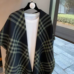 Detail view of a stylish black and green plaid winter cape shawl displayed on a hanger.