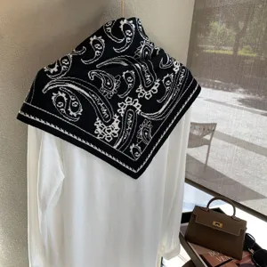 Vista detallada de panuelo triangular de punto paisley negro y blanco en parte superior.