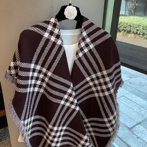 Detailed view of a stylish brown and white plaid knitted shawl with fringe hem, elegant winter cape.