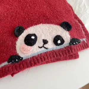 Close-up view of the cute cartoon panda embroidery on the soft red knitted winter scarf fabric.