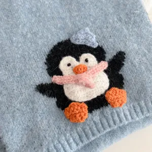 Close-up detail of the cute crochet penguin patch on the light blue knit scarf, soft winter warm.