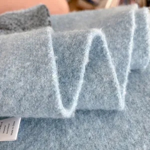 Close-up detail shot of a soft light blue fuzzy knitted wool blend scarf cozy texture.