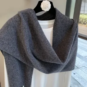 Detailed view of a dark grey knitted wool shawl scarf draped over a clean white inner garment.