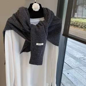 Close-up detail of the dark grey wool knit shawl draped over a white long sleeve top.