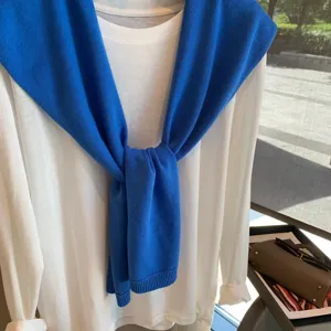 Close-up of stylish white long-sleeve t-shirt with royal blue knitted shawl draped.