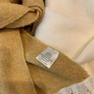 Close-up detail of soft knitted scarf with lace edge and fabric composition tag.