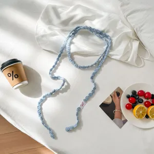 Detailed view of handmade light blue crochet long scarf or necklace accessory on white bed.