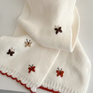Close-up detail of a soft white knit scarf featuring cute embroidered butterflies.