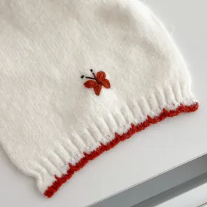 Close-up detail of a white knitted winter scarf featuring a cute embroidered butterfly and red edge.