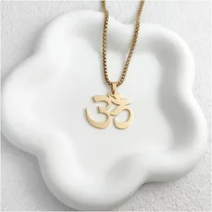 Primer plano de collar con colgante OM dorado en bandeja blanca, joyería de yoga espiritual
