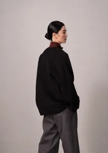 Detailed shot of a stylish black short coat paired with a brown turtleneck and grey trousers.