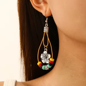 Nahaufnahme des bohemian Ohrrings mit bunten Perlen, Metallblume und gelber Kordel.