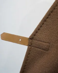 Close-up detail of brown cashmere short coat featuring a stylish leather strap and fine stitching.