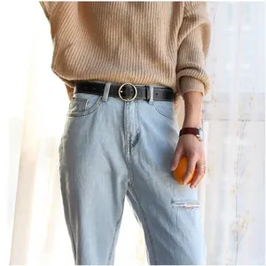 Detailed shot of a classic black leather belt with a round metal buckle worn with jeans.