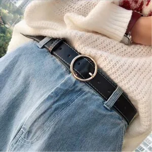 Close-up detail shot of a classic black leather belt with a round gold buckle on blue jeans.