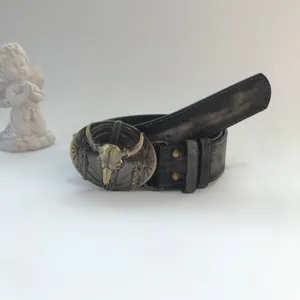 Detail view of a vintage western leather belt featuring a bold metal bull skull buckle design.