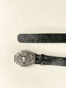 Gros plan sur la boucle de ceinture tête de taureau western et la lanière en cuir gaufré.