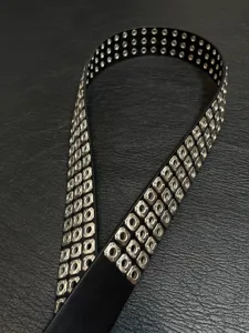 Closeup detail of black punk rock leather belt featuring double rows of square metal eyelets.