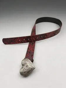 Close-up detail of vintage western leather belt showing floral emboss pattern and heart buckle.