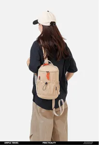 Back view of a compact khaki canvas backpack worn by a model, showing multi-way straps and details.